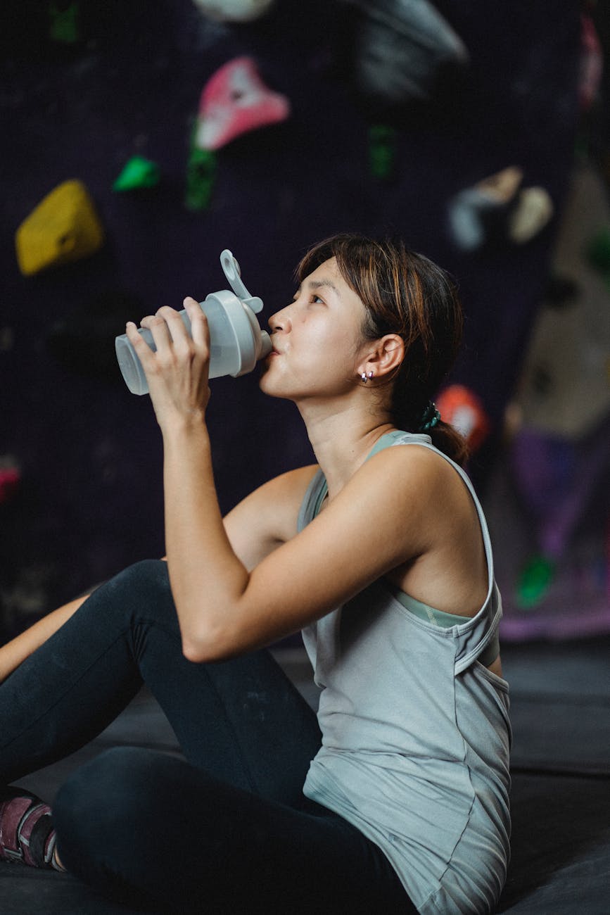 thirsty ethnic sportswoman drinking water after bouldering workout